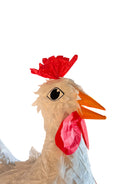 A white chicken pinata with red comb and wattles, and orange beak and legs, standing upright.