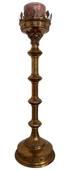 A tall, ornate, antique brass or bronze Gothic church candlestick holder with a pink candle in the top.