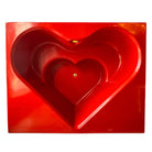 A top-down, straight-on view of a vintage, high-gloss cherry red bathtub. The tub basin is molded into a distinct double-tiered heart shape, with a shallower outer heart cascading into a deeper, smaller inner heart basin centered within a wide rectangular red deck.