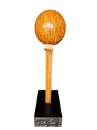 A wooden sculpture featuring a dark square base, a vertical trunk that branches into two angled supports, and a turned wooden sphere resting on the higher support.