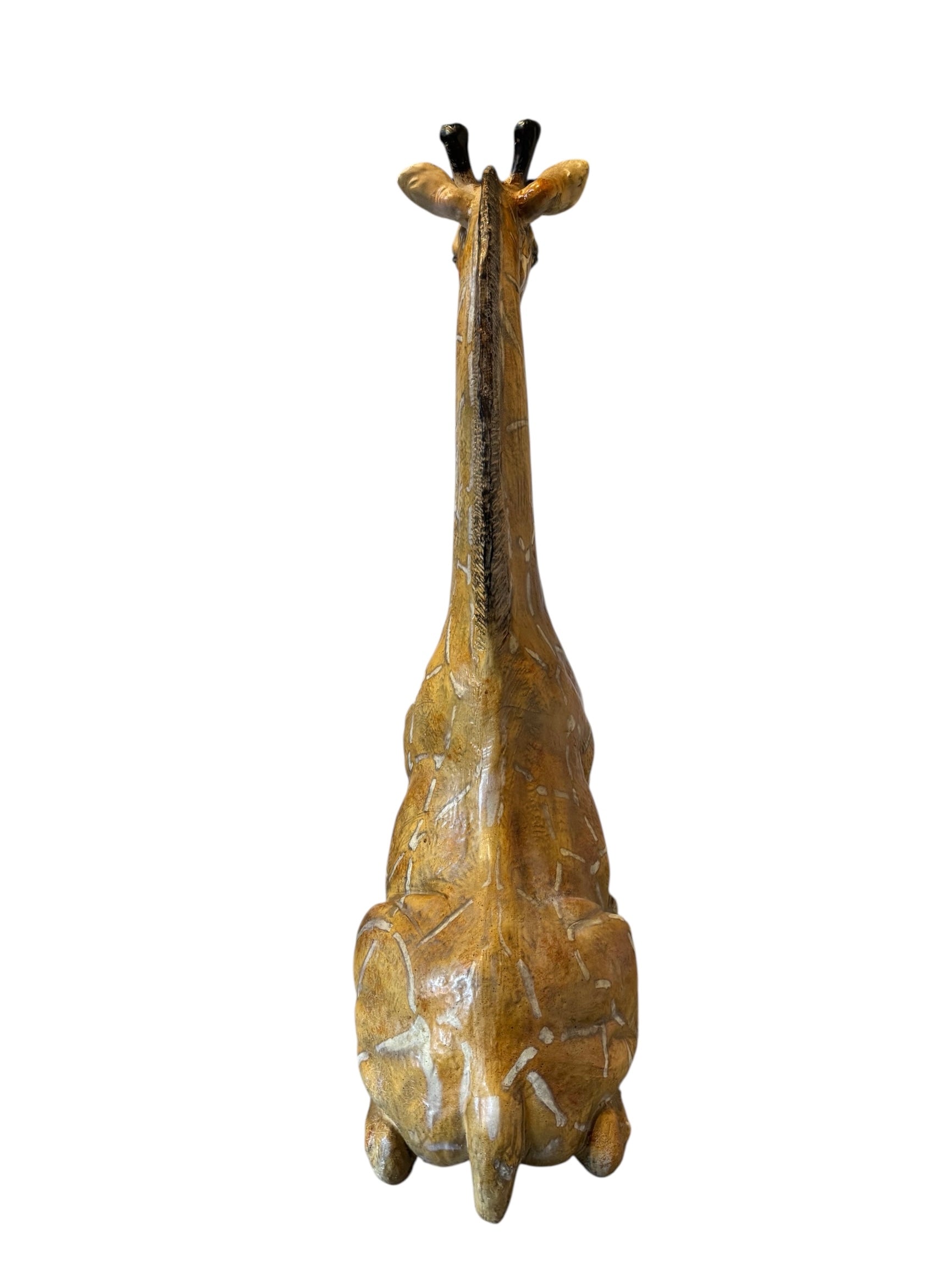 A hand-painted, cast resin sculpture of a seated giraffe. The giraffe has a long neck, is predominantly gold with light markings, and is in a resting pose. The sculpture is against a plain white background