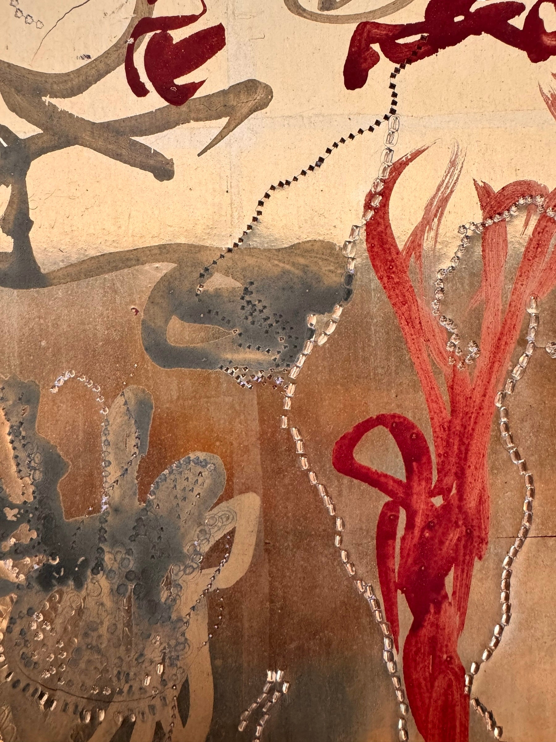 A vertical abstract work on a weathered gold-leaf panel. The upper section features bold, dark red calligraphic symbols resembling distorted kanji or script. Below, delicate, dotted white lines wind through the composition like strings of pearls or constellations. A slender, vertical form in vibrant red stands on the right, while muted, smoky-grey washes of paint ground the bottom of the piece.