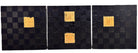 A triptych of abstract paintings featuring a grid pattern of textured black squares by Sabine Stromeyer called “Square One”. The left and right panels each have a single vertical gold rectangle in the center, while the middle panel has two stacked gold rectangles in the center.