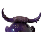 Glossy purple ceramic sculpture featuring a round body and stylized bull horns adorned with rings, and a nose ring. The sculpture has no eyes, but suggests a smiling expression.