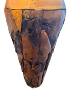Two table lamps made from repurposed teak wood vases. The bases are tall and tapered, featuring a rugged, mosaic-like texture composed of various pieces of dark, polished teak wood with visible natural grain and crevices. Each lamp is topped with a large, warm-toned conical shade that is currently wrapped in protective clear plastic, emitting a soft, golden glow. The lamps are positioned on a clean white surface against a neutral background.
