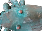 A green and red, glazed ceramic platter in the shape of a prickly pear cactus pad with attached prickly pear fruit. The surface has raised dots representing spines. 