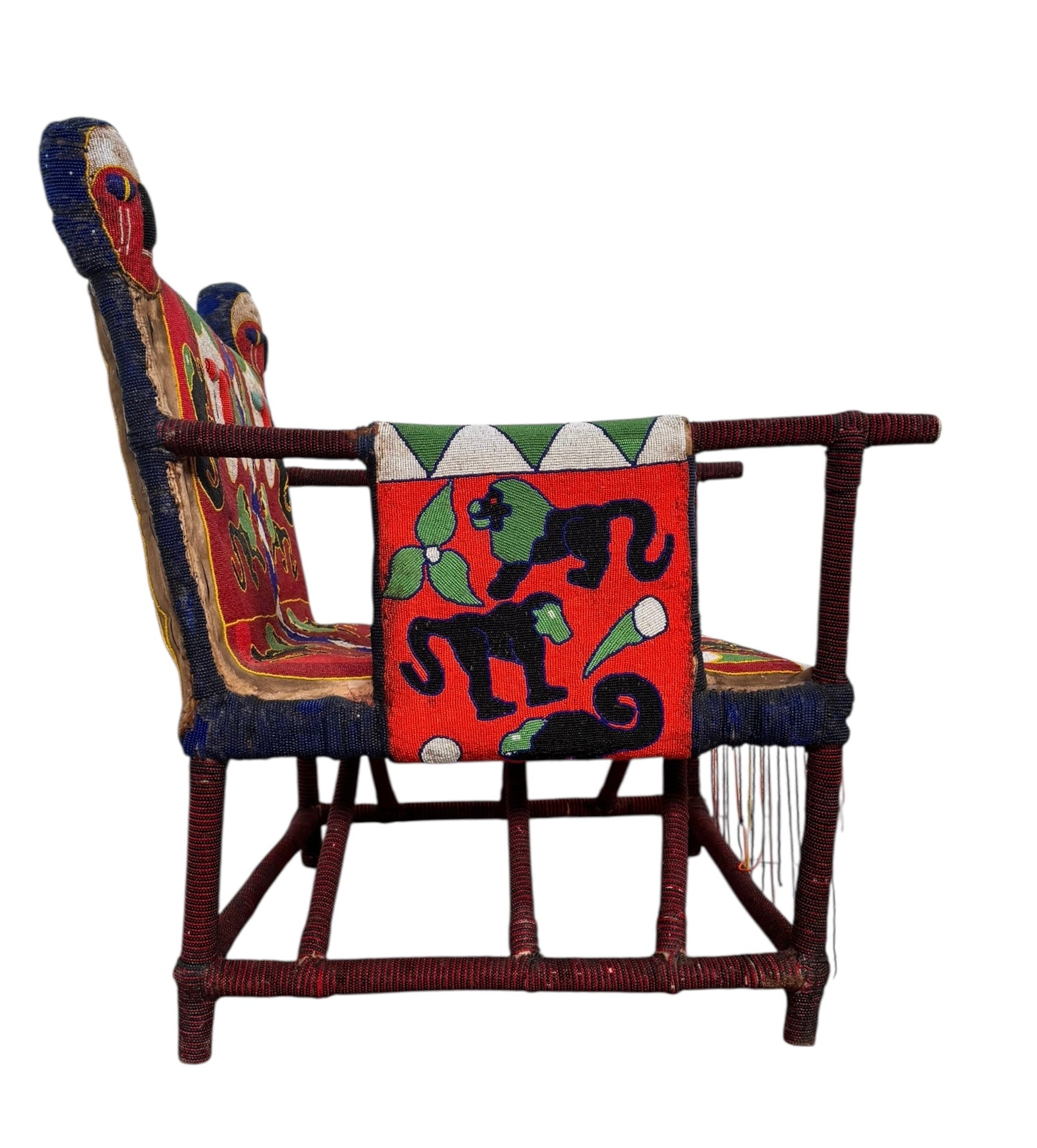 Close-up of a Yoruba beaded armchair, featuring vibrant red, blue, and green beads in a pattern of stylized masks and animals such as lions and zebras