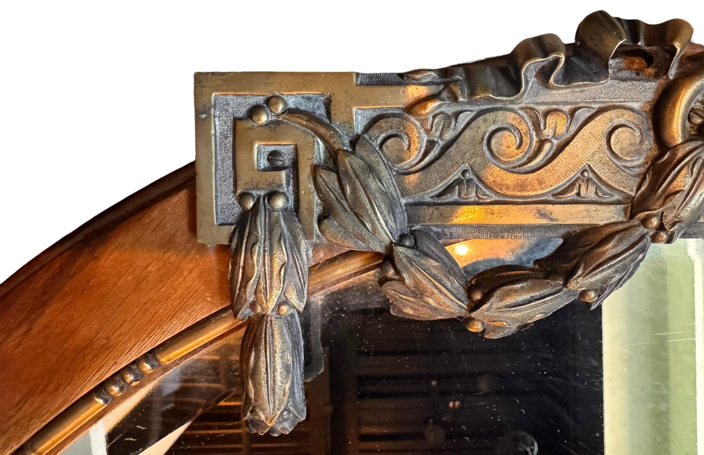 An oval-shaped mirror featuring a wooden frame and an ornate metal crest at the top.