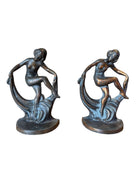 Two cast iron bookends in the Art Deco style. Each features a nude female figure leaning gracefully with one leg extended, posed atop a stylized wave or drape. The bookends have a bronze-colored finish and a vintage appearance.
Bronze Echoes: Art Deco Bookends attributed to Hubley Mold