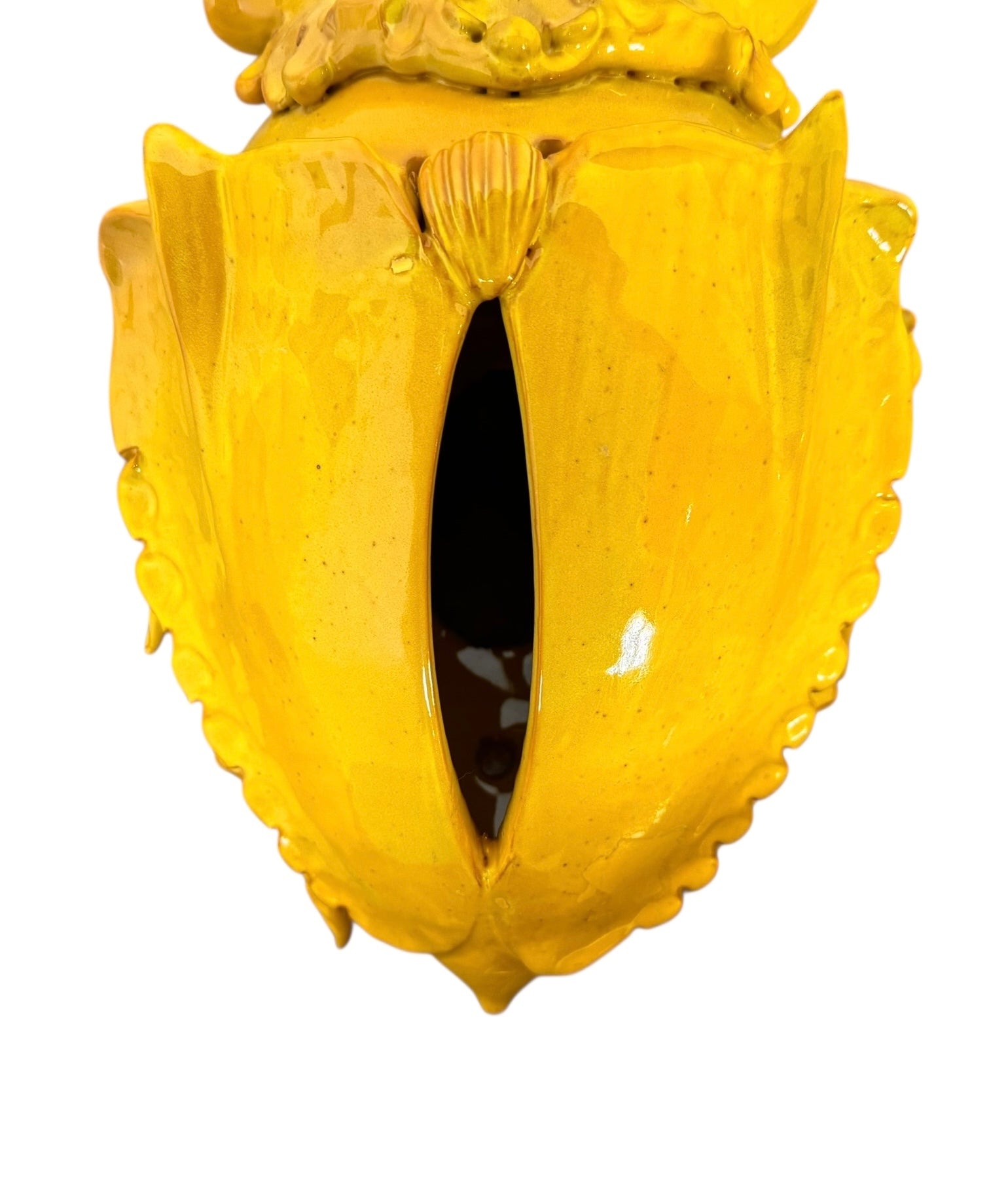 a large, high-gloss ceramic sculpture by Enza Fasano, shaped like a stylized beetle. The entire piece is finished in a warm, honey-yellow glaze. The beetle features prominent, curved mandibles at the front, a textured "collar" area, and a rounded, shell-like body with decorative ridges along the edges. The surface is smooth and reflective, catching the light across its organic contours.