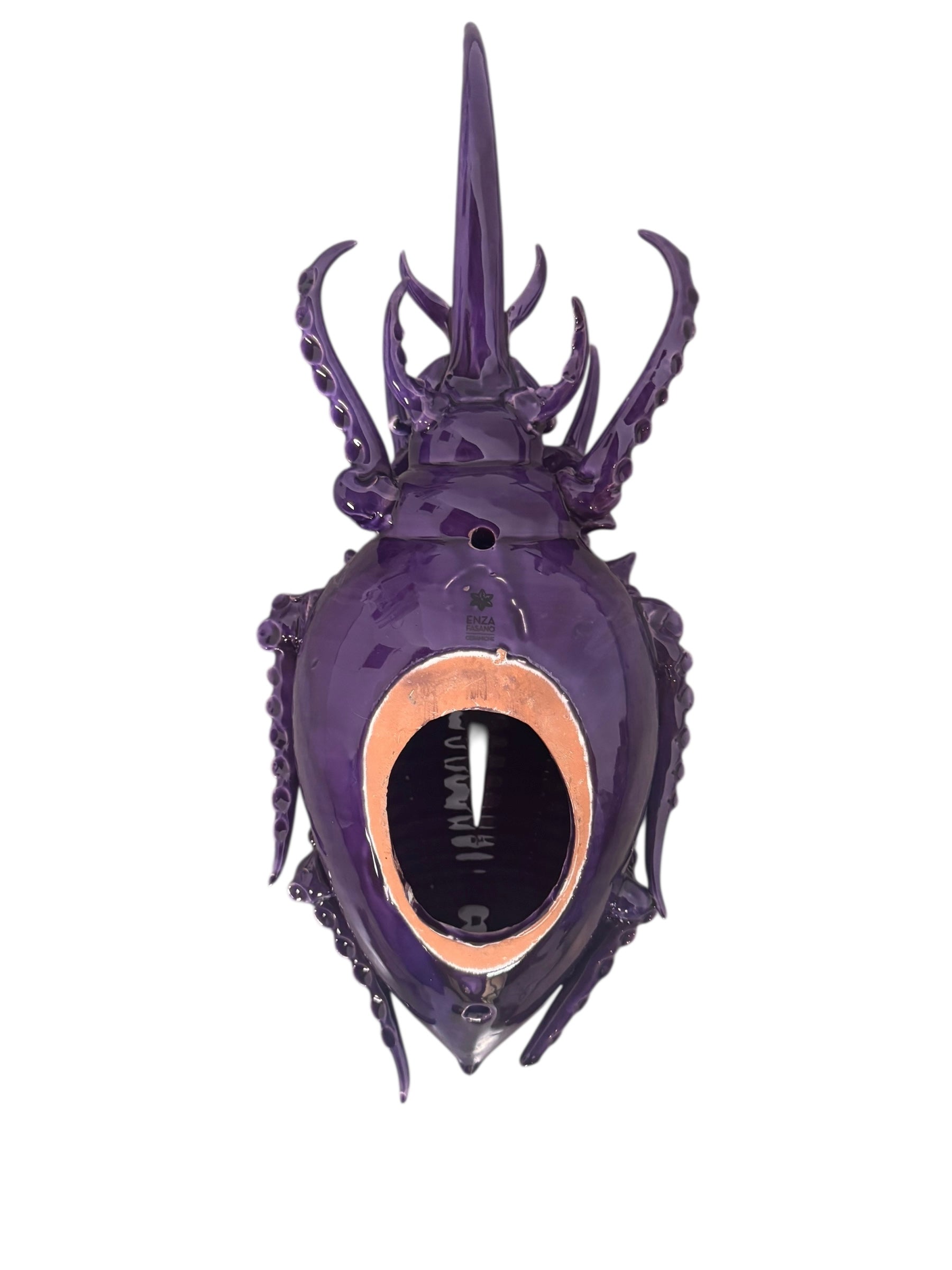A glossy, deep purple ceramic sculpture of a beetle by Enza Fasano. The piece features a highly stylized and ornate design, blending insect-like anatomy with fantastical elements. It has a smooth, rounded shell and elongated, curved mandibles and appendages lined with sharp, thorn-like protrusions. The monochromatic glaze is reflective, highlighting the intricate sculptural details and textures of the avant-garde artwork.