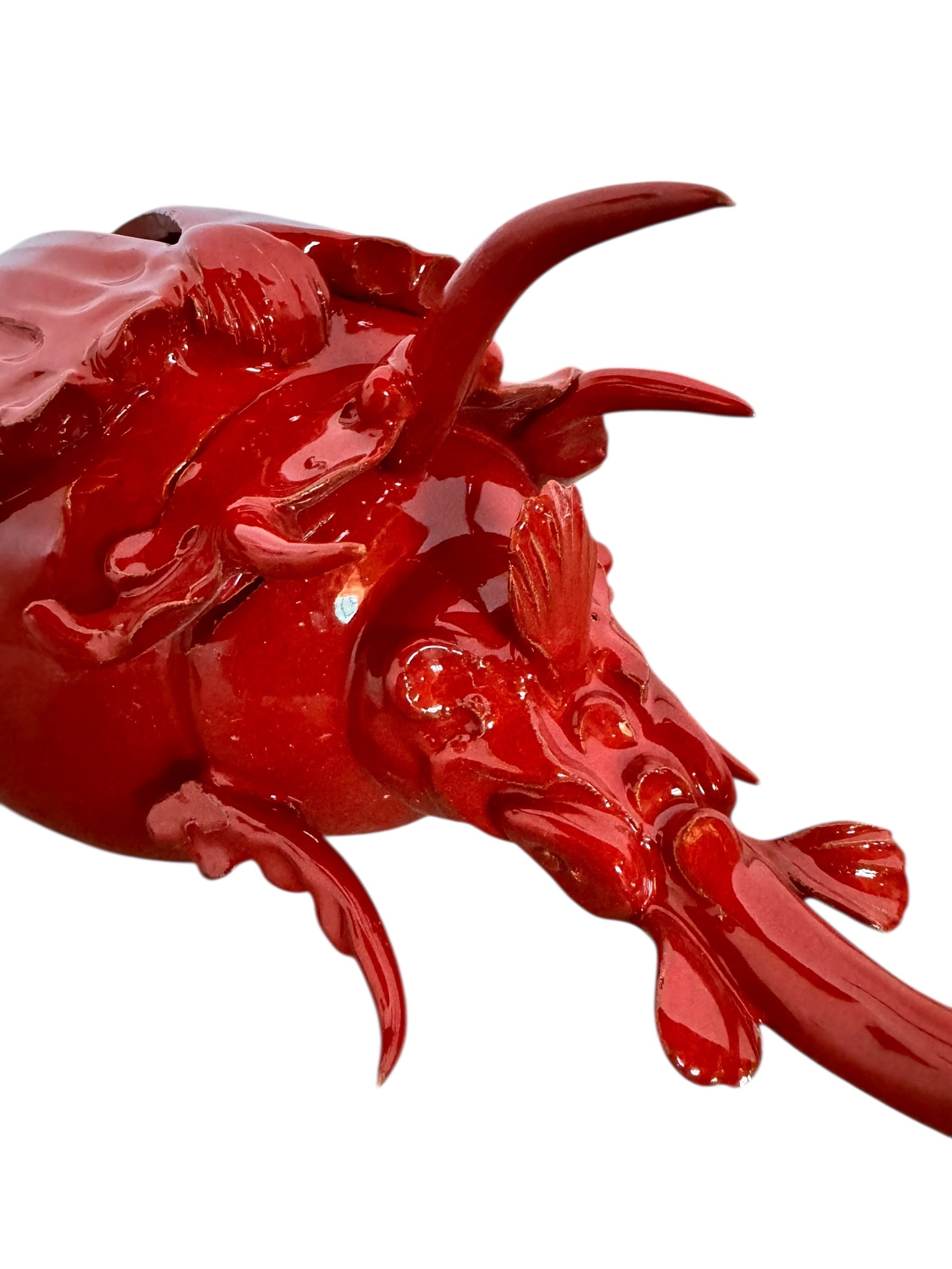 A vibrant, glossy red ceramic sculpture of a rhinoceros beetle by Enza Fasano. The piece features a highly reflective, deep crimson glaze that accentuates its smooth, rounded abdomen and the intricate, jagged textures of its head and horns.
