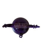 Glossy purple ceramic sculpture featuring a round body and stylized bull horns adorned with rings, and a nose ring. The sculpture has no eyes, but suggests a smiling expression.