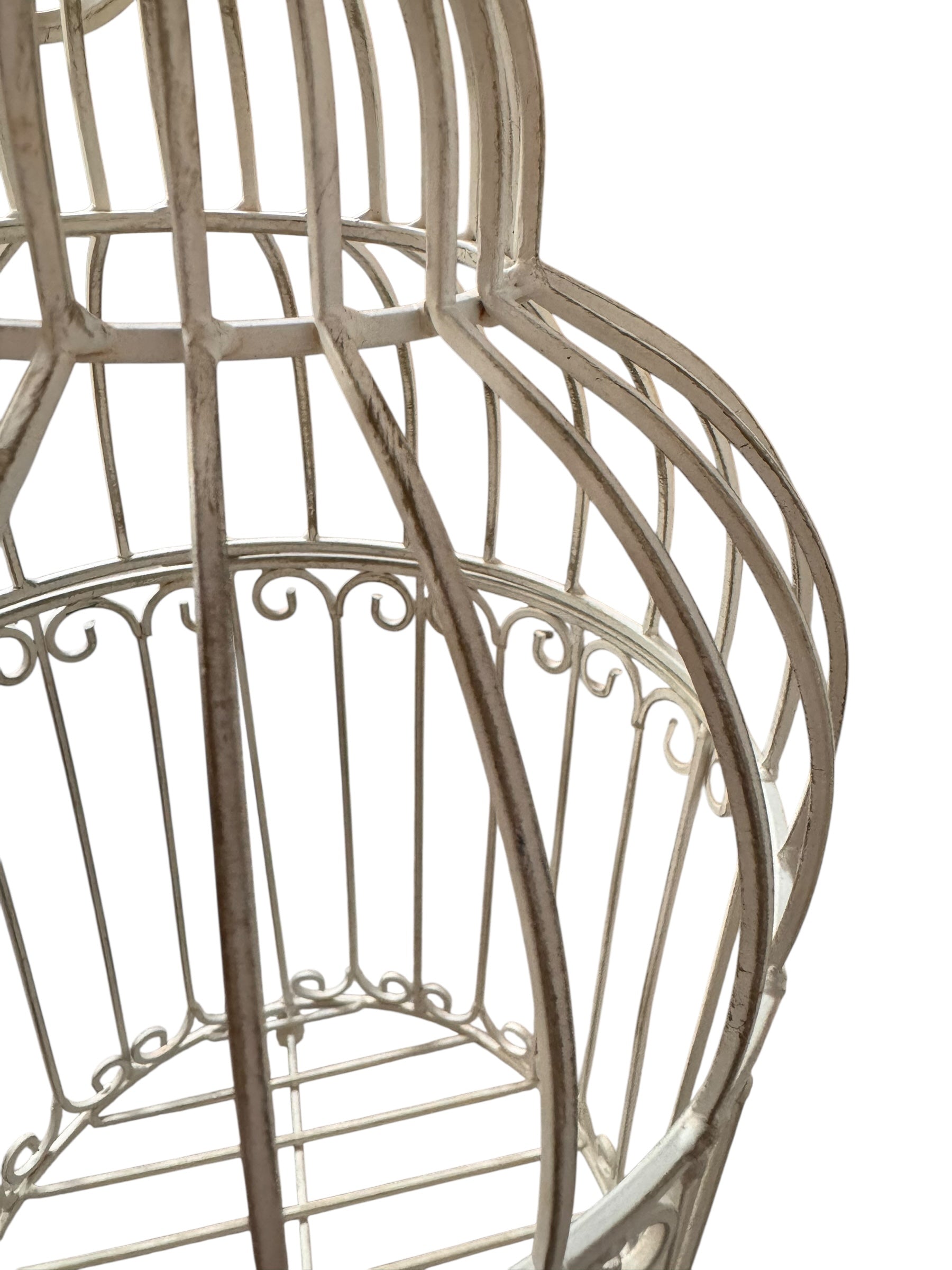 A single, white or cream-colored, decorative wrought iron bird cage with a hinged door and a hanging loop at the top. The cage has a vintage or antique style 