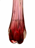 A table lamp featuring a teardrop-shaped, reddish-purple glass base and a conical, pleated, light-pink fabric shade.