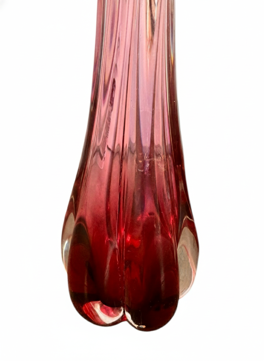 A table lamp featuring a teardrop-shaped, reddish-purple glass base and a conical, pleated, light-pink fabric shade.