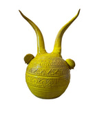 Yellow ceramic sculpture titled 'The Ram Oracle' by Enza Fasano, featuring a round body with intricate, hand-incised patterns and long, stylized ram-like horns