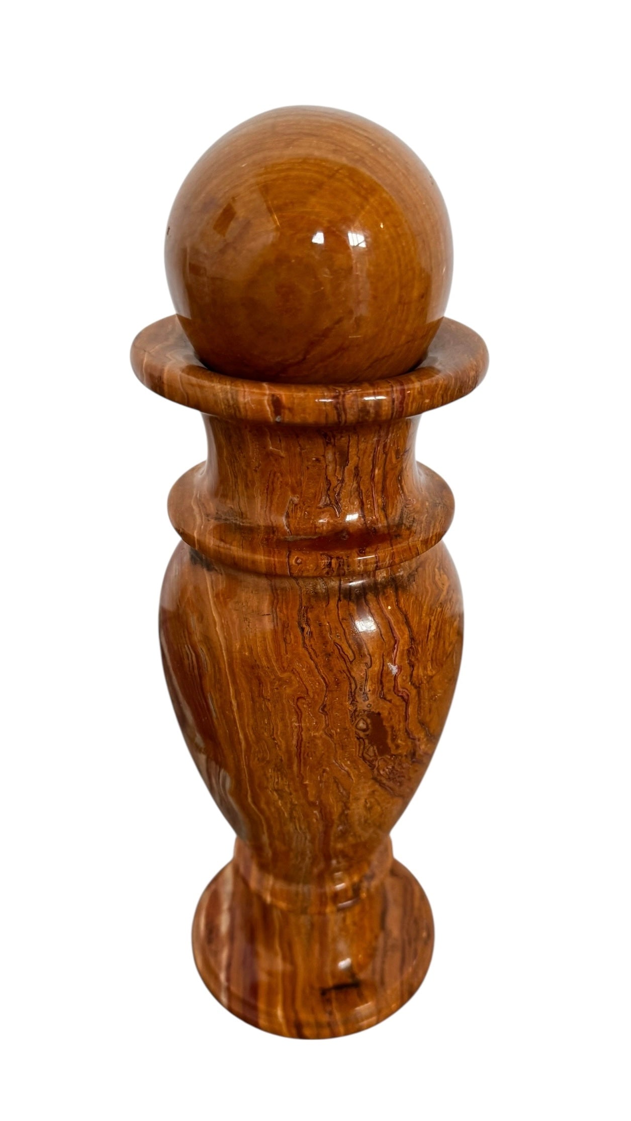 An elegant, hand-carved decorative vase made of polished Pakistani brown onyx. The vase features a classic, rounded urn shape with a tiered, flared neck and a solid matching spherical stone stopper resting on top. The stone displays rich, natural horizontal banding and swirling patterns in shades of honey, deep amber, rust-red, and cream. It stands on a small, integrated pedestal base against a clean white background, reflecting a high-gloss, mirror-like finish.