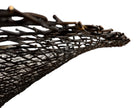 A round metal wall sculpture by Michael Aram, viewed from the front against a stark white background. The piece is composed of a dense, intricate lattice of fine, dark metal wire or twigs woven together to create a textured, web-like pattern. The structure curves inward like a funnel or a vortex, sloping down toward a clean, circular opening in the exact center, creating a strong sense of depth and dimensionality.