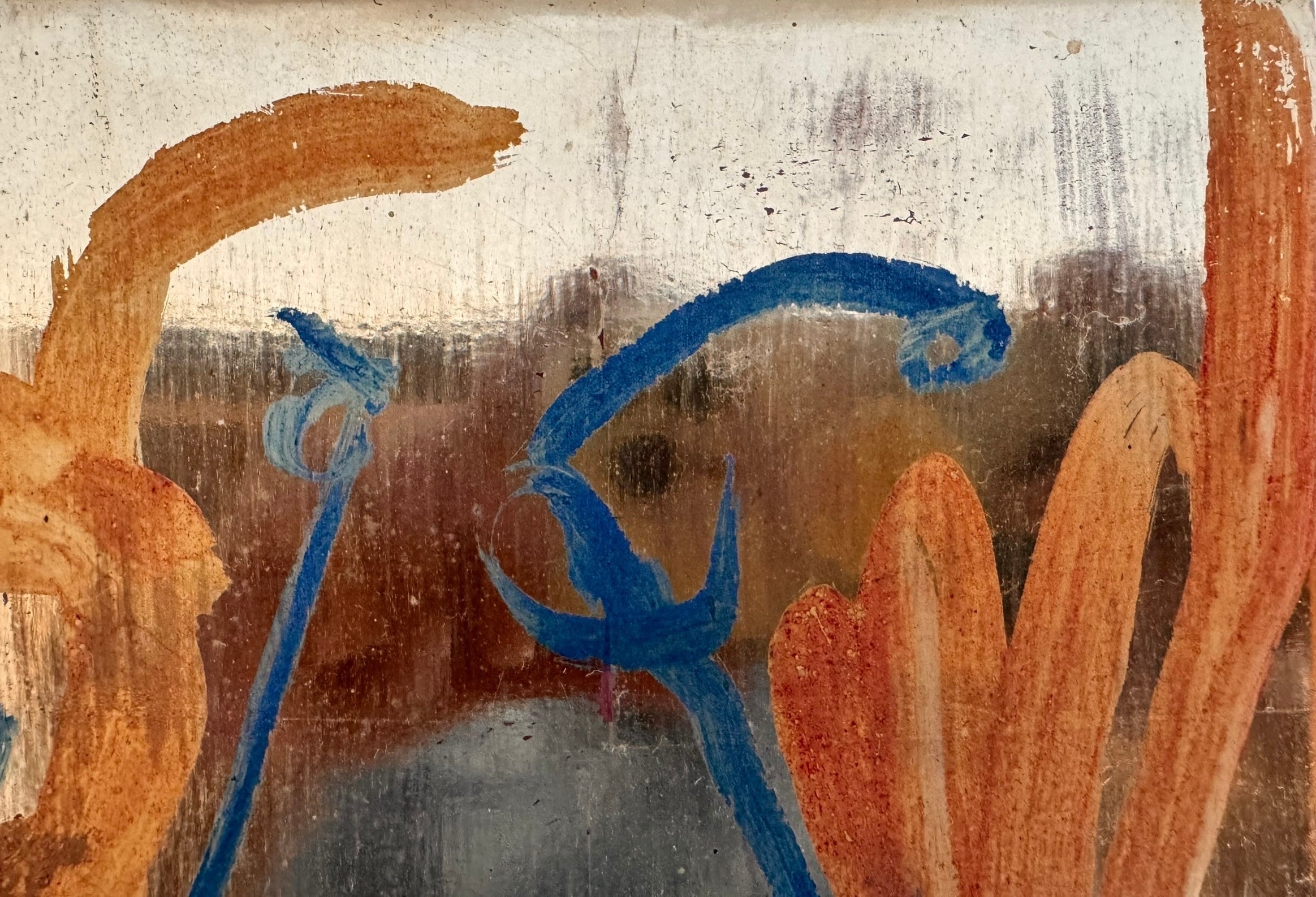 An abstract mixed-media painting on a vertical rectangular panel with a reflective, metallic gold and copper background. The composition features fluid, expressive brushstrokes in warm orange, ochre, and deep blue.
The orange strokes are thick and organic, resembling swirling flames or floral petals, while the blue marks consist of thin, lyrical lines and looped scribbles that dance across the surface. The metallic substrate is visible through the translucent paint, creating a play of light and texture