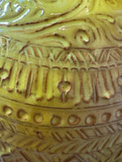 Yellow ceramic sculpture titled 'The Ram Oracle' by Enza Fasano, featuring a round body with intricate, hand-incised patterns and long, stylized ram-like horns
