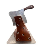 A wooden sculpture with a highly polished, reddish-brown grain, featuring two main asymmetrical, curved sections that converge at the top. Circular metal inlays with black centers are embedded across the surface of both wooden sections. A flat, polished metal blade-like element is inserted vertically between the two wooden sections, extending above the top surface. The sculpture rests on a metallic base.