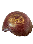 A handcrafted Murano glass bowl with a ruffled edge, deep red color, and gold specks created using the "oro zecchino" technique. The surface has a crackled gold pattern that reflects light, making it a striking decorative piece.
