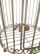 A single, white or cream-colored, decorative wrought iron bird cage with a hinged door and a hanging loop at the top. The cage has a vintage or antique style 