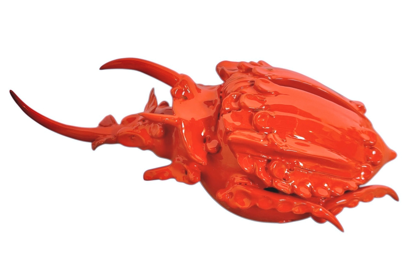 A glossy, vibrant orange ceramic sculpture of a rhinoceros beetle by Enza Fasano. The piece features a highly polished, reflective glaze and stylized, fluid anatomical details. Its prominent dual horns curve forward, and the body is textured with layered, wing-like plates, set against a plain white background.