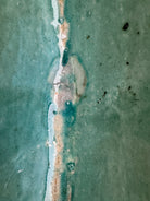 curved ceramic piece resembling a green pod, supported by a block plinth. The seafoam-green ceramic structure extends wide on either side, curving upward to form a wavy, boat-like shape. The outer surface is dotted with rows of small, raised, brown-orange, acorn-like protrusions. The top rim is layered with parallel, grooved ridges. The base is a vertical rectangular block with a heavily textured, bark-like surface in a dark green and black finish.