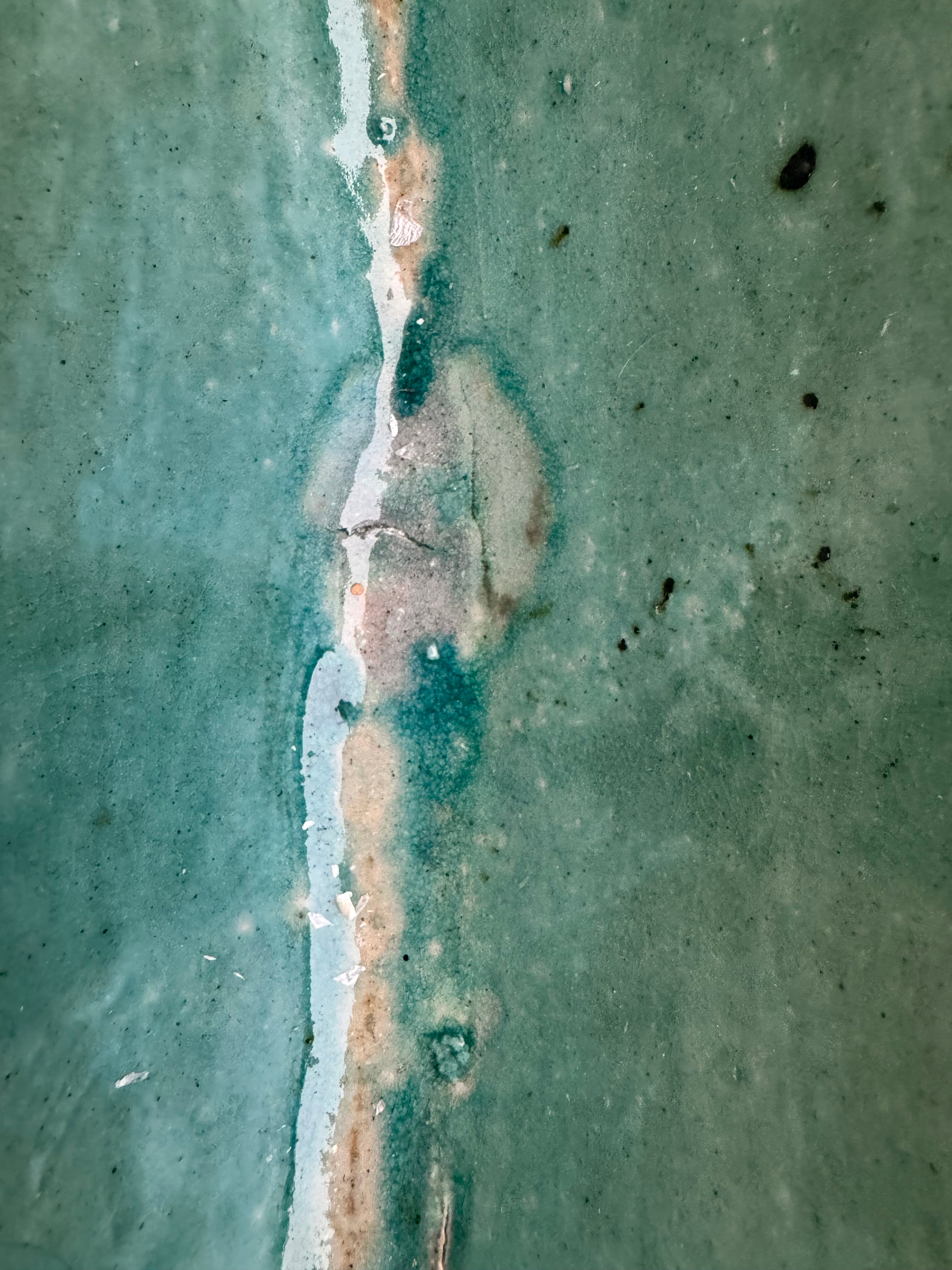 curved ceramic piece resembling a green pod, supported by a block plinth. The seafoam-green ceramic structure extends wide on either side, curving upward to form a wavy, boat-like shape. The outer surface is dotted with rows of small, raised, brown-orange, acorn-like protrusions. The top rim is layered with parallel, grooved ridges. The base is a vertical rectangular block with a heavily textured, bark-like surface in a dark green and black finish.