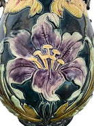 An ornate, dark glazed ceramic Art Nouveau vase with two handles and raised floral designs in yellow, purple, and green.