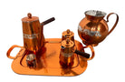 The set includes a large, rectangular, hammered copper tray with geometric openwork handles. Resting on the tray is a tall, slightly tapered copper coffee pot with a wooden handle, a matching smaller creamer pitcher with a similar wooden handle, a lidded sugar bowl, and a tiny matching metal cup or jigger. To the right off the tray sits a large, spherical copper water pitcher or jug with a wide mouth and ice lip.