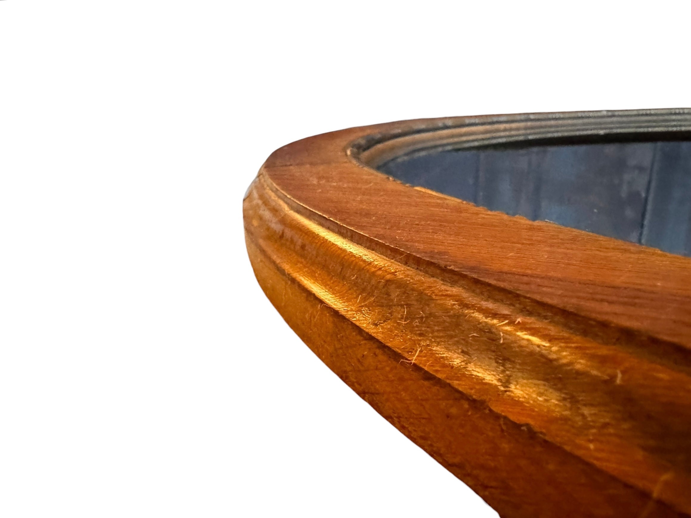 An oval-shaped mirror featuring a wooden frame and an ornate metal crest at the top.