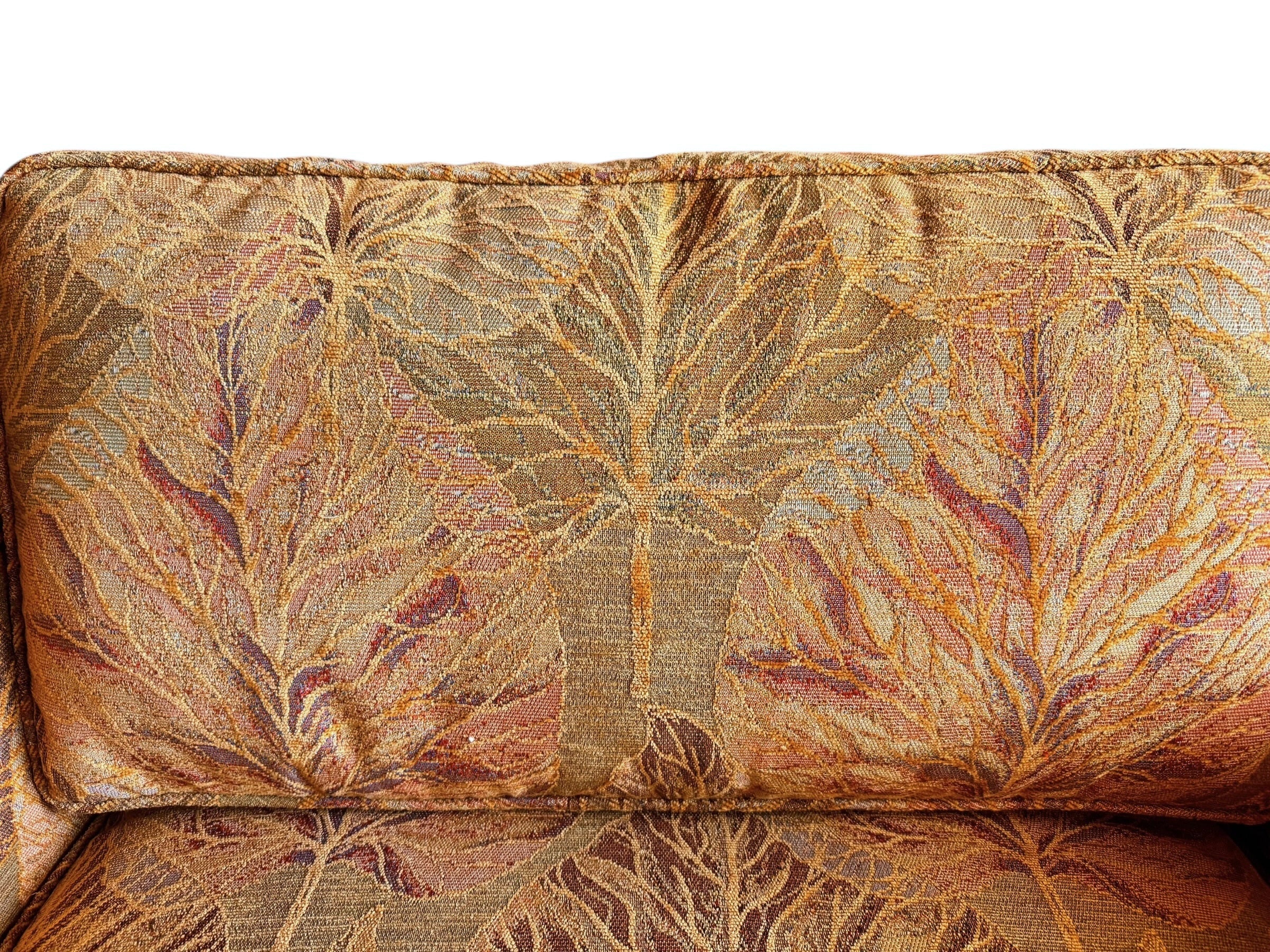 A Neoclassical-style wooden loveseat with a dark mahogany frame featuring scrolled arms and tapered legs. The upholstery consists of plush cushions and two matching cylindrical bolster pillows, all covered in a golden-yellow jacquard fabric with a large-scale, repeating autumnal leaf pattern in shades of muted orange and brown.