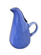A Russel Wright American Modern stoneware water pitcher in a glossy Manitoga blue glaze is centered against a white background. The pitcher has a teardrop shape, a large handle, and a wide spout