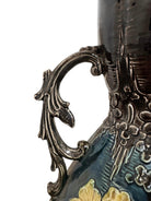 An ornate, dark glazed ceramic Art Nouveau vase with two handles and raised floral designs in yellow, purple, and green.