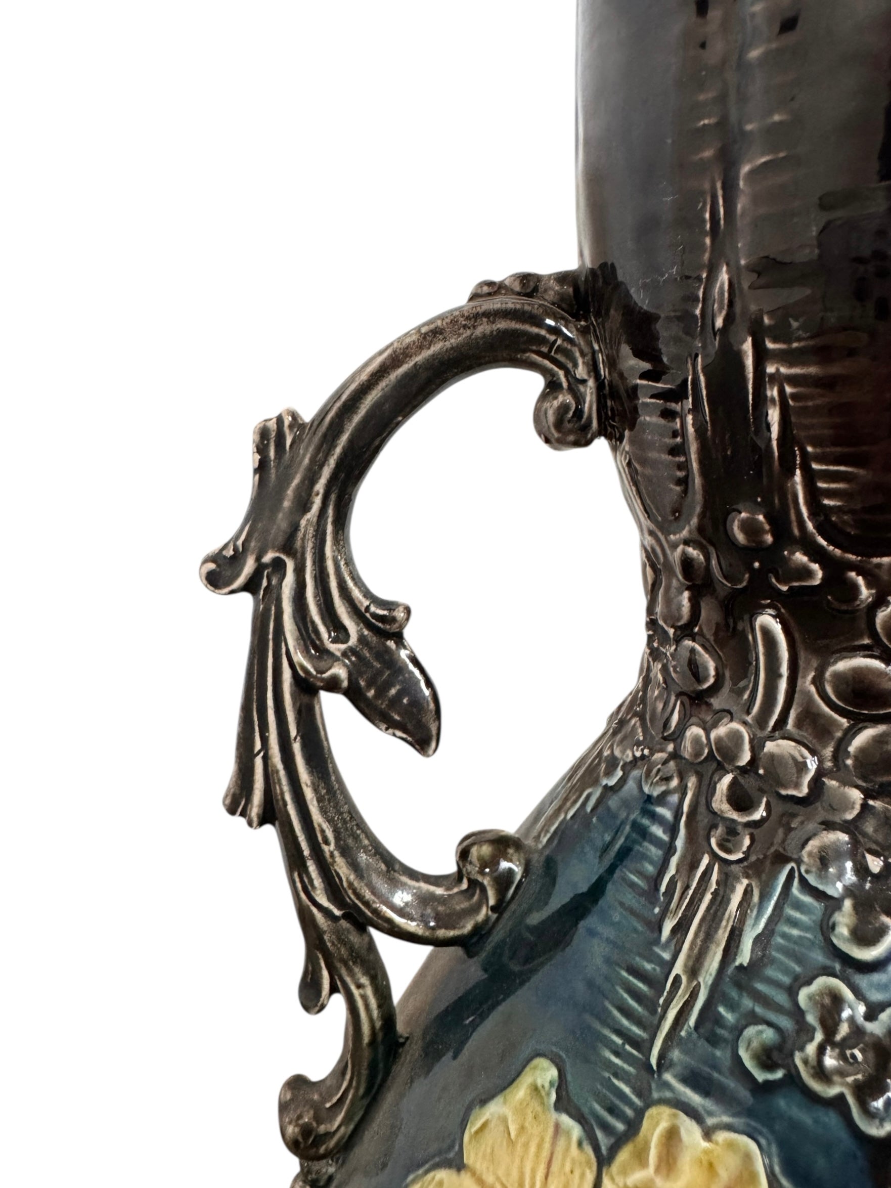 An ornate, dark glazed ceramic Art Nouveau vase with two handles and raised floral designs in yellow, purple, and green.