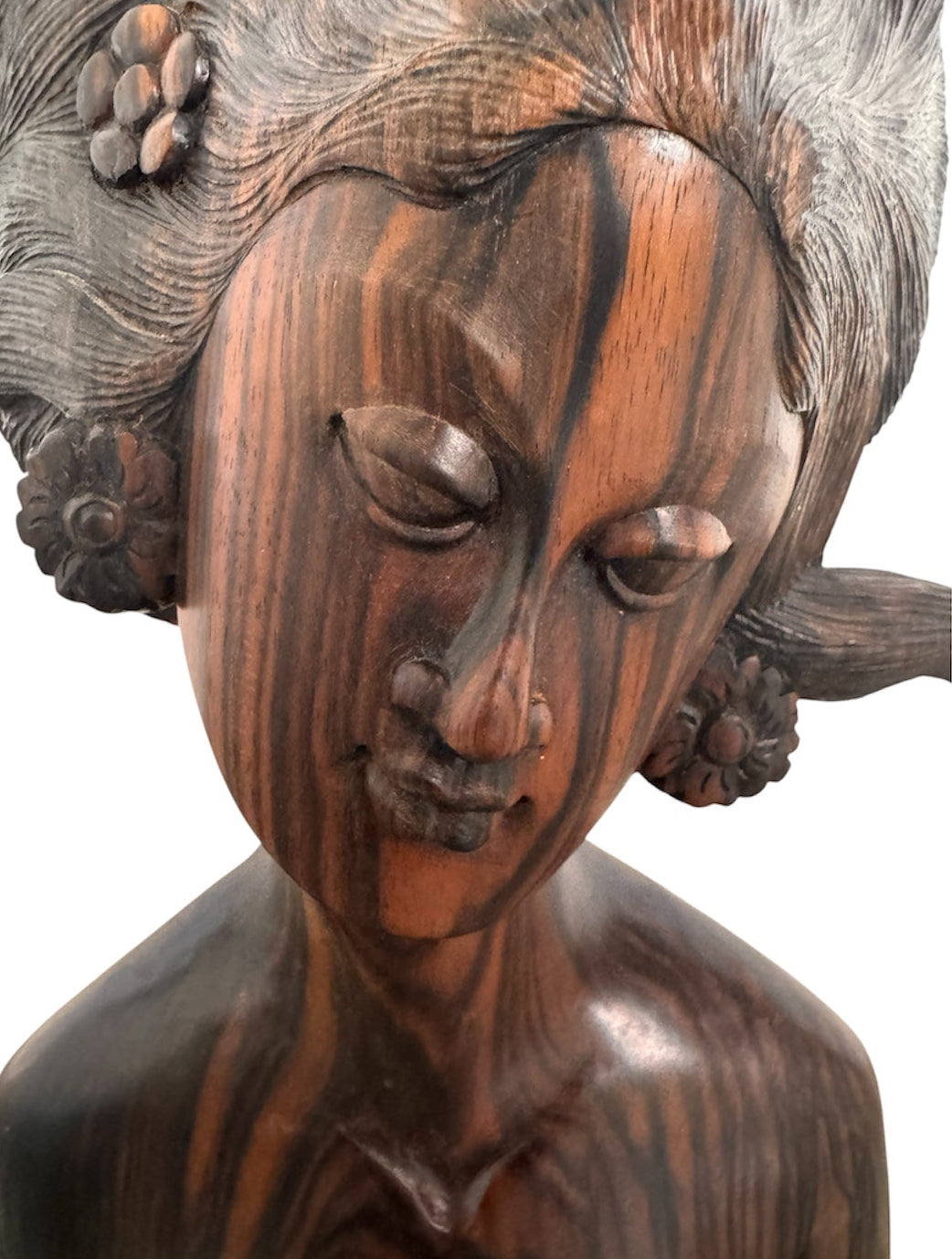 An elegant hand-carved bust of a woman made from rich, polished dark ebony wood with striking reddish-brown grain patterns running vertically through her face and chest. The sculpture features a serene expression with closed eyes, a slender nose, and relaxed lips. Her voluminous, textured hair rises upward in a Fan-like shape, intricately carved with fine lines and adorned with small, delicate flower details. The bust includes her bare shoulders and upper chest, resting on a flat base.