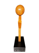 A wooden sculpture featuring a dark square base, a vertical trunk that branches into two angled supports, and a turned wooden sphere resting on the higher support.