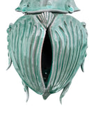A ceramic sculpture of a stylized beetle by Enza Fasano, featuring a deep emerald green glaze with dark, metallic bronze-colored accents. The beetle is depicted with a highly textured, ribbed shell (elytra) and prominent, curved horns. Its legs are stylized with suckers, reminiscent of octopus tentacles. The piece has a glossy finish and rests against a plain white background.