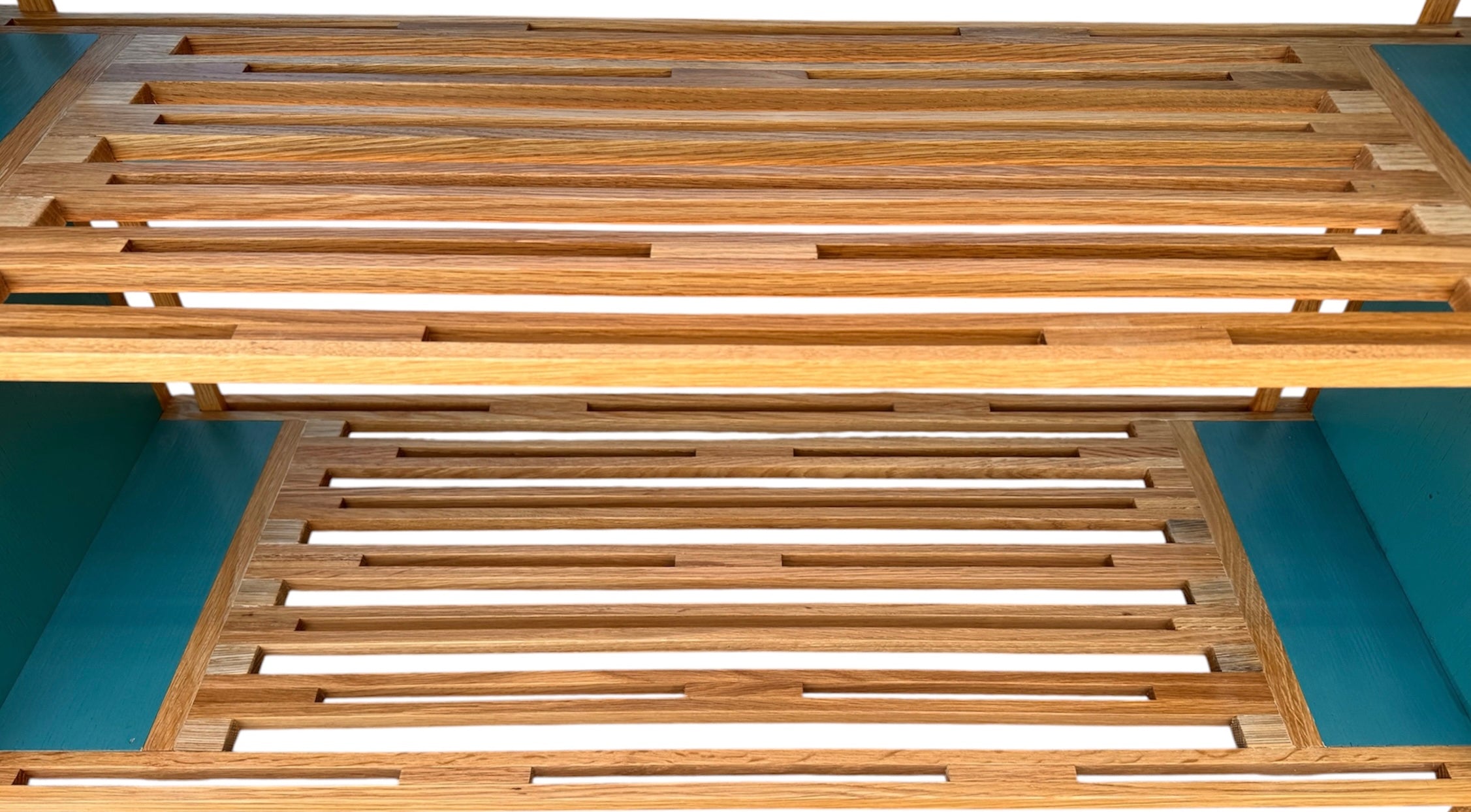 A three-tiered wooden shelving unit featuring a mix of light oak and teal-colored panels. The piece has an open, structural design with visible joinery, vertical supports that extend past the top shelf, and a horizontal backrest at the top. The middle and bottom shelves feature slatted wood center sections flanked by solid teal panels, while the top surface is primarily solid wood with teal accents at the edges.