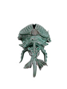 A ceramic sculpture of a stylized beetle by Enza Fasano, featuring a deep emerald green glaze with dark, metallic bronze-colored accents. The beetle is depicted with a highly textured, ribbed shell (elytra) and prominent, curved horns. Its legs are stylized with suckers, reminiscent of octopus tentacles. The piece has a glossy finish and rests against a plain white background.