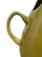 A chartreuse (yellow-green) ceramic pitcher designed by Russel Wright, featuring a teardrop shape, an elongated spout, and a curved handle