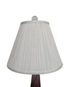 A tall, Mid-Century Modern sculptural table lamp featuring a hand-blown art glass base. The base is crafted in the Sommerso style, with a deep amethyst purple core encased in a thick, clear crystal outer layer that twists upward in an organic, fluid motion. The lamp is topped with a white, knife-pleated empire shade and a clear glass ball finial. The overall design is elegant and slender, emphasizing the contrast between the saturated purple glass and the transparent, light-refracting crystal.
