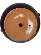 Glossy purple ceramic sculpture featuring a round body and stylized bull horns adorned with rings, and a nose ring. The sculpture has no eyes, but suggests a smiling expression.