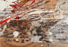 horizontal rectangular mixed media abstract artwork by J. Rogers, dated 2010, presented in a thin black frame. The composition is set against a light-toned wood grain background and features a dynamic, gestural arrangement of thick white impasto, splatters of red and black paint, and aggressive black scribbles. A vertical strip of textured material is collaged near the center, while various washes of tan and cream create a sense of weathered depth across the wooden surface.