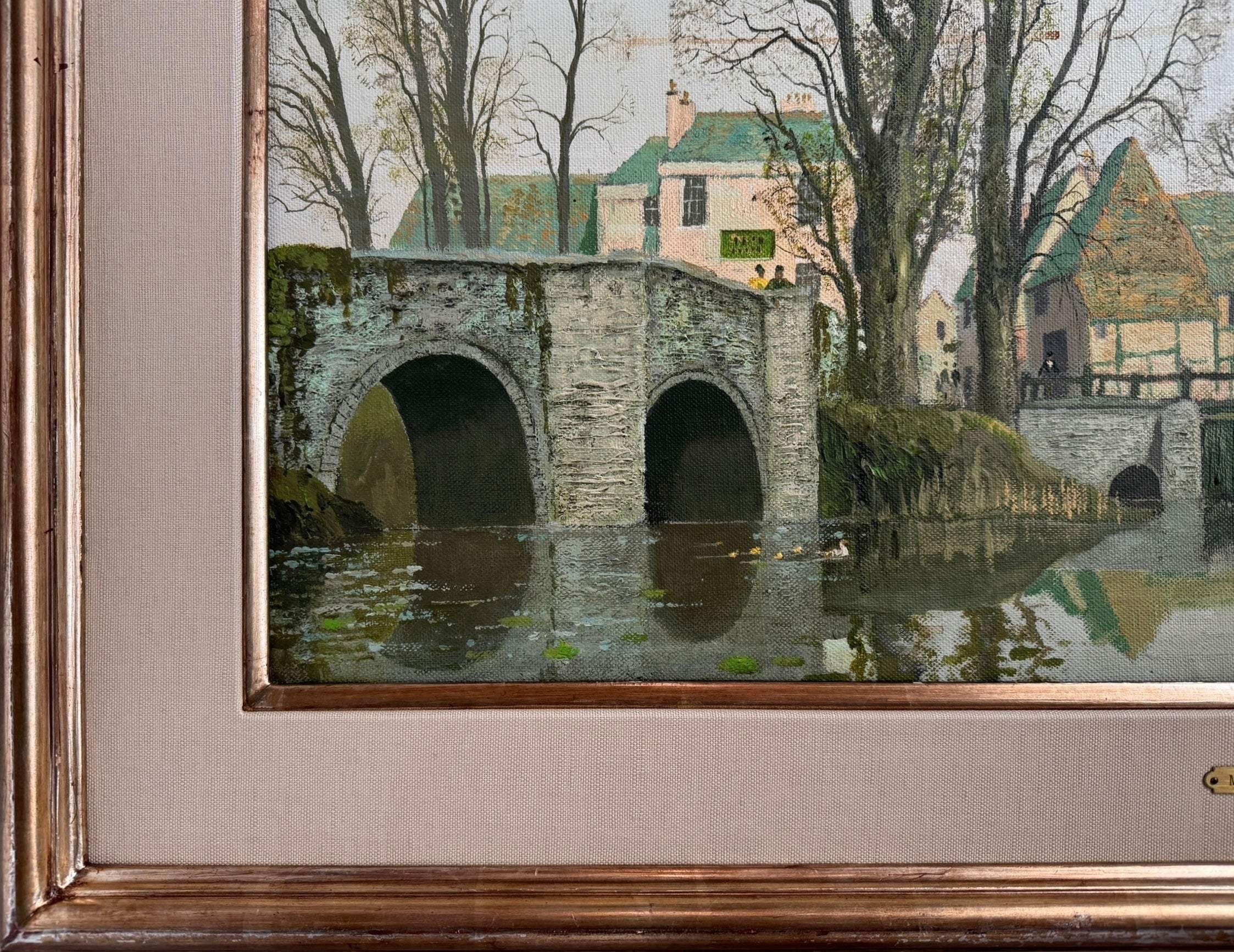 A naturalistic landscape oil painting by Michael Reilly titled "Mill Pond with Bridge" depicts a small town scene with a stone bridge over a mill pond, several buildings, and numerous bare trees under a grey sky