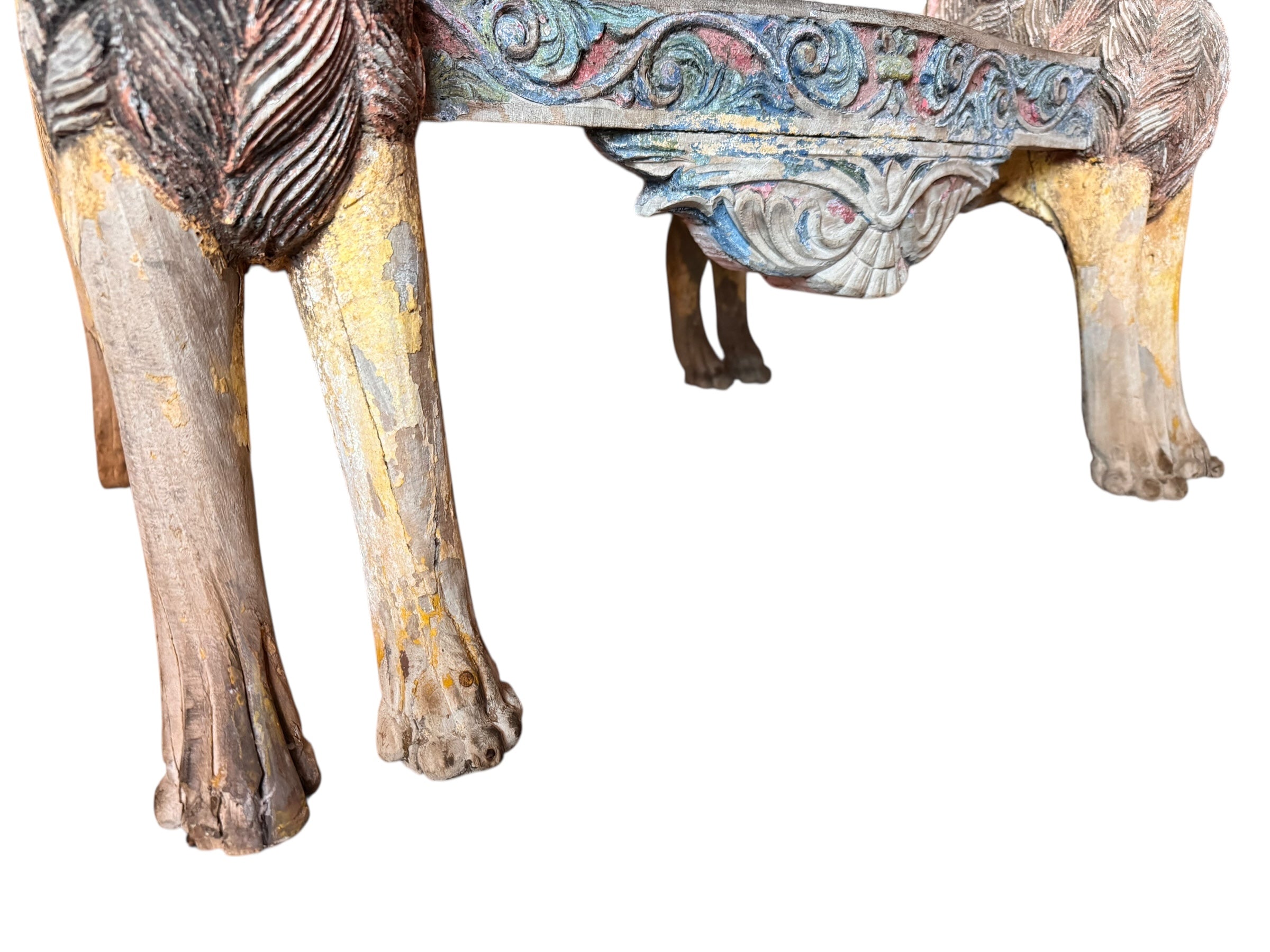 A pair of antique, heavily carved Anglo-Indian style throne chairs featuring lion figures as legs and arm supports, and peacock motifs on the backrests. The chairs have a distressed, multi-colored painted finish.