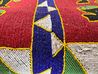 Close-up of a Yoruba beaded armchair, featuring vibrant red, blue, and green beads in a pattern of stylized masks and animals such as lions and zebras